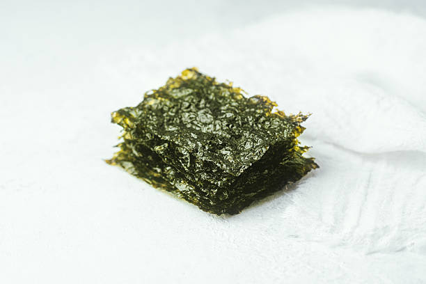 istock Crispy seaweed snack in white bowl with loose piece on light background 2216420510