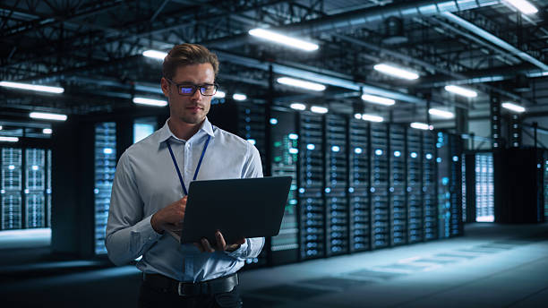 istock Technology Research Facility: Male Project Manager Standing at the Corridor and Uses Tablet Computer. Engineers or Developers Work on Engine Design and Use Digital Computers 2216425465