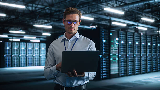 istock Successful Male Data Center IT Specialist Look Attentively at Laptop Computer Screen, while Work with Server Farm Cloud Computing Facility. System Engineer Working for Cyber Data Security Company. 2216425493