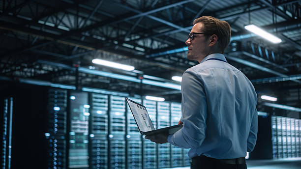 istock Creative Caucasian Man Using a Laptop Computer in Evening Office. Independent Businessman is Walking Through the Office and Looking Away. Technology Science Breakethrough, Progress, Innovation Concept 2216425511