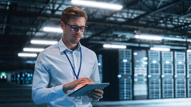 istock Data Center Male e-Business Entrepreneur Use Tablet Computer. Information Technology Professional on Bridge Overlooking Big Cloud Computing Server Farm. Analytics Concept 2216426075