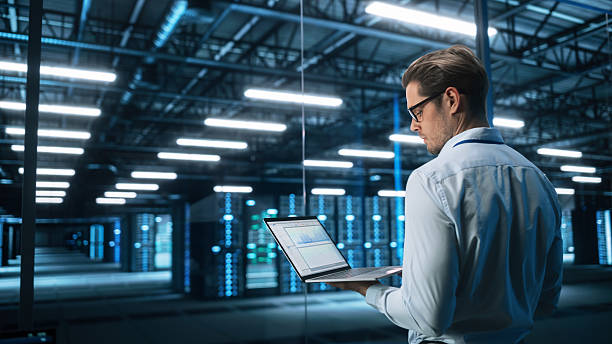 istock Portrait of IT Specialist Uses Laptop in Data Center. Server Farm Cloud Computing Facility with Male Maintenance Administrator Working. Cyber Security and Network Protection 2216426376