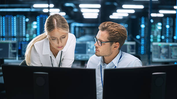 istock Businessman Uses Desktop Computer, while Consults with Female Project Manager about work issues In the Big Corporate Firm Office at the Background. Businesspeople concept 2216426733