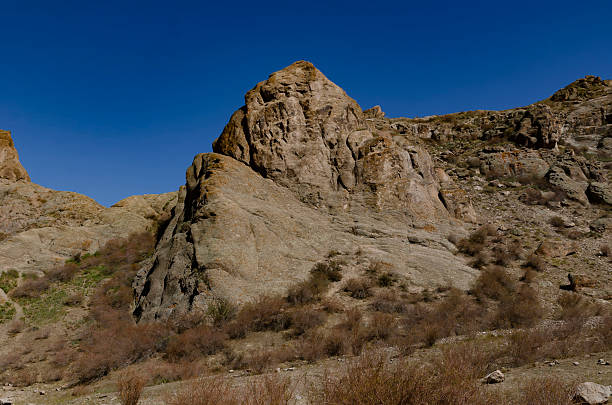 Massive Rock Formation in Dry Mountain Valley under Clear Deep Blue Sky with Sparse Vegetation.