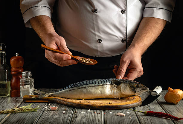 istock A chef is seasoning a fresh mackerel fish using a wooden spoon to sprinkle spices. The rustic kitchen atmosphere features ingredients like salt, pepper, and onion 2216427246
