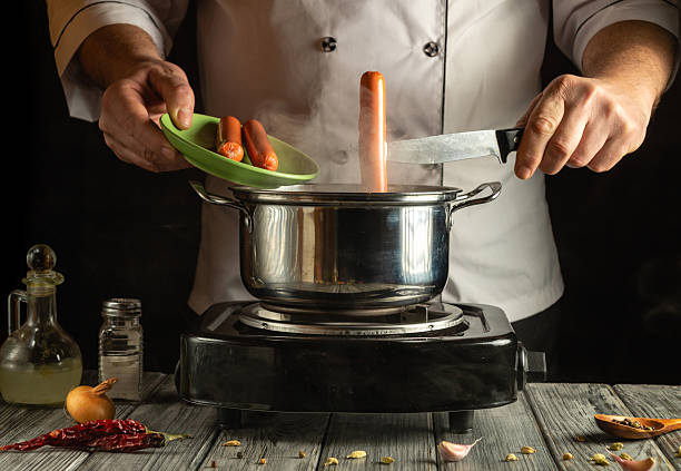 istock In a warm kitchen setting, a chef skillfully prepares sausages, adding them to a simmering pot. The atmosphere is vibrant with ingredients and culinary tools scattered around 2216427307
