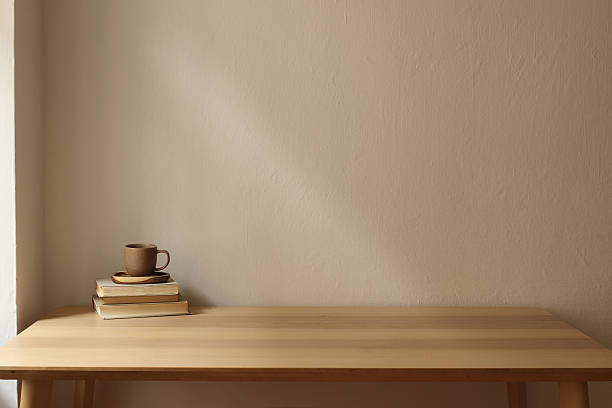 Minimalist elegant interior. Wooden table, stacked vintage books and ceramic coffee, tea cup. Soft natural light, plain beige wall background. Calm cozy atmosphere. Empty copy space. Breakfast concept