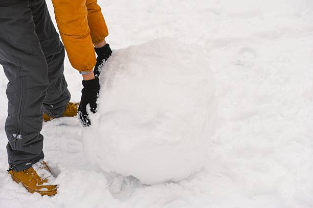 istock Child pushing a large snowball in the snow 2216429346