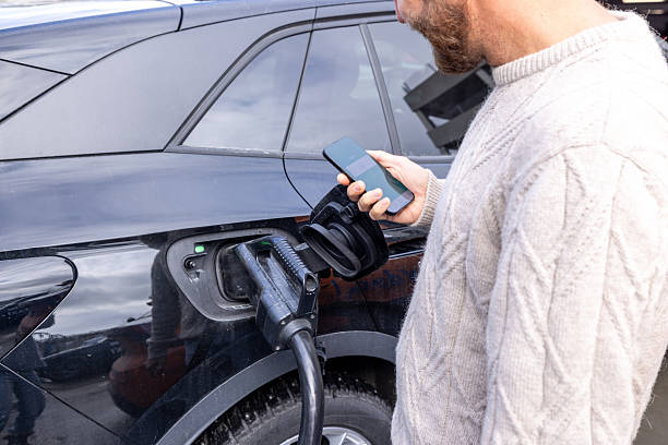 istock Man Charging Electric Car While Holding Smartphone 2216467679