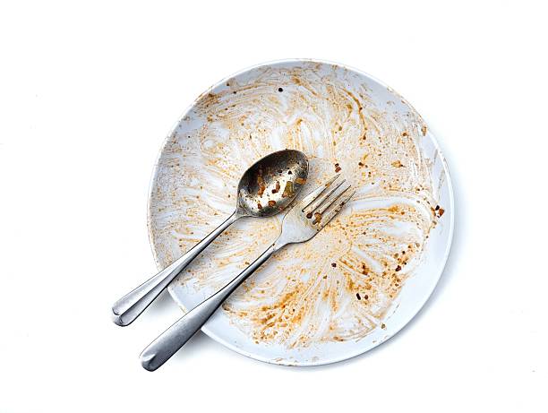 istock Dirty white plate with leftovers food with spoon and fork on top isolated on white background 2216473751
