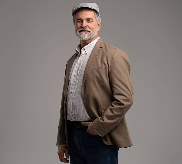 Attractive serious grey-haired man in suit and flat cap isolated on grey background