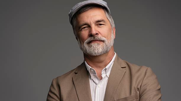 Attractive serious grey-haired man in suit and flat cap isolated on grey background