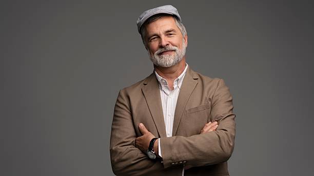 istock Attractive serious grey-haired man in suit and flat cap isolated on grey 2216484331