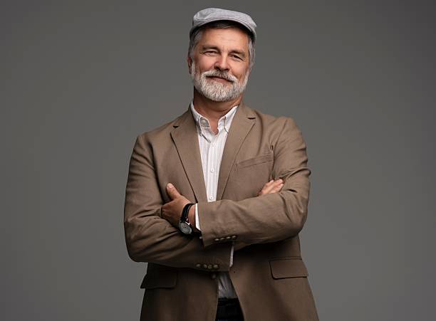 istock Attractive serious grey-haired man in suit and flat cap isolated on grey 2216484343