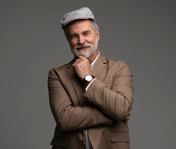 istock Attractive serious grey-haired man in suit and flat cap isolated on grey 2216484347