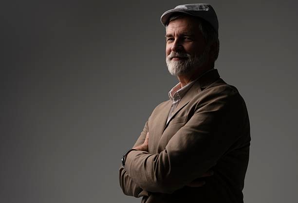 Men's beauty, fashion. Retro style. Mature handsome man in suit and flat cap on grey background.