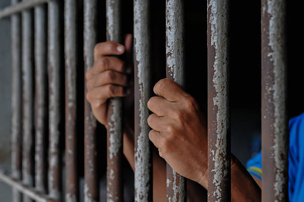 istock hands of a prisoner behind prison bars on black background 2216491078