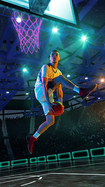 istock Hand made collage. Player in white uniform leaps under glowing violet hoop in 3D arena with neon lights, starry ceiling and illuminated court. 2216491588
