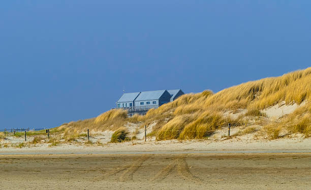 noordwijk, Netherlands – December 07, 2021: A vertical shot of a lone house at the a grassy beach against a blue sky in The Netherland