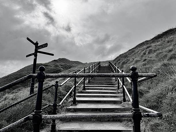 An empty outdoor staircase with railings and directional signs against cloudscape