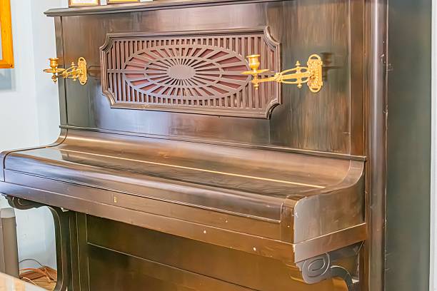 istock Centrally placed grand piano possibly black or deep brown with a lighter body, positioned in a dim room Intricate metalwork detail on top, keys with classic layout white and black, pedalboard, o 2216498428