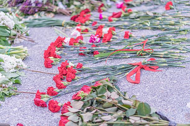 istock Flowers on a concrete monument, primarily red carnations and white roses Freshly cut bunches, with some greenery interspersed Tight clusters in foreground, spreading out towards background Natural 2216498461