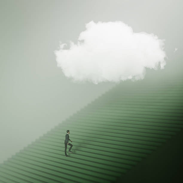 istock A man climbing a huge staircase in misty atmosphere with a cloud hovering above symbolizing the long journey and the achievement. 2216499207