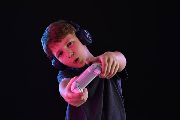 istock Cute little boy in headphones playing video game with controller on black background 2216499655