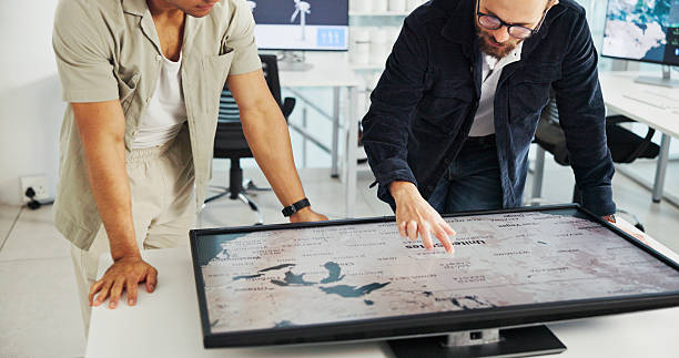 Engineer, people and hands with world map on screen for turbine location, power development and data analysis. Interactive display, teamwork and employee pointing to chart area for site selection