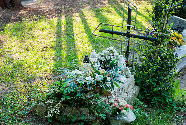 Serene Catholic cemetery with rustic iron cross and lush floral tributes in peaceful sunlit setting featuring greenery and floral arrangements