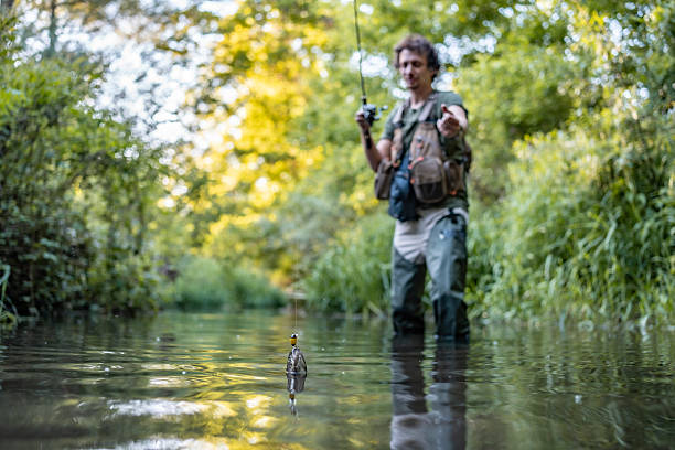 A man immersed in fishing activities on a scenic river amidst lush greenery in daylight, showcasing the tranquility and skill involved in this popular outdoor hobby.