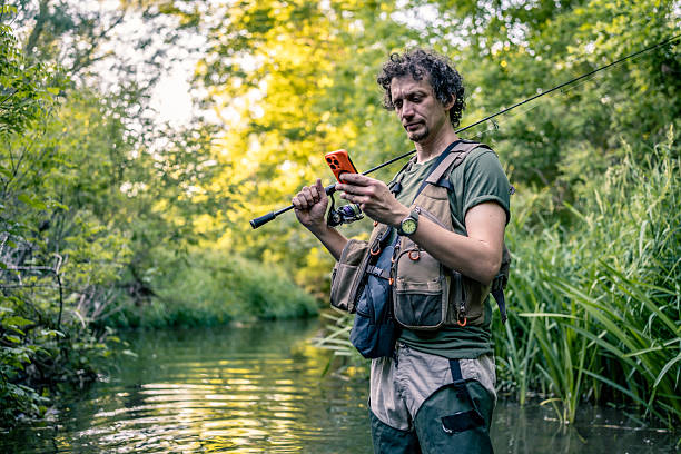 istock Man Fishing in Stream Using Smartphone Amid a Scenic Natural Background 2216515357