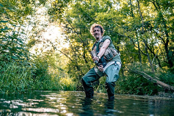 Outdoor enthusiast fly fishing in a lush forest stream during a sunny, peaceful afternoon.