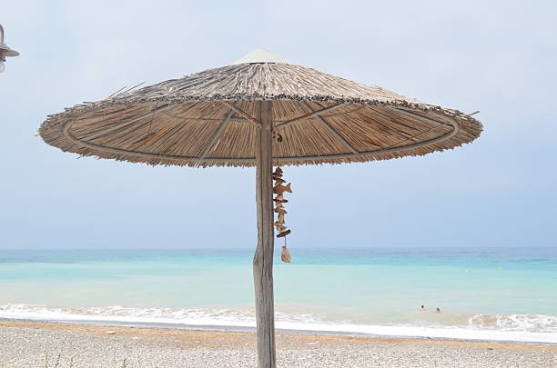 Sunny beach with straw umbrella overlooking turquoise sea.