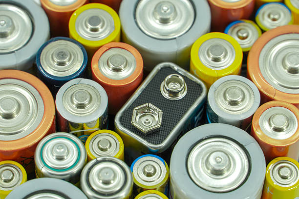 Background made of various alkaline and lithium-ion batteries, positive pole visible.