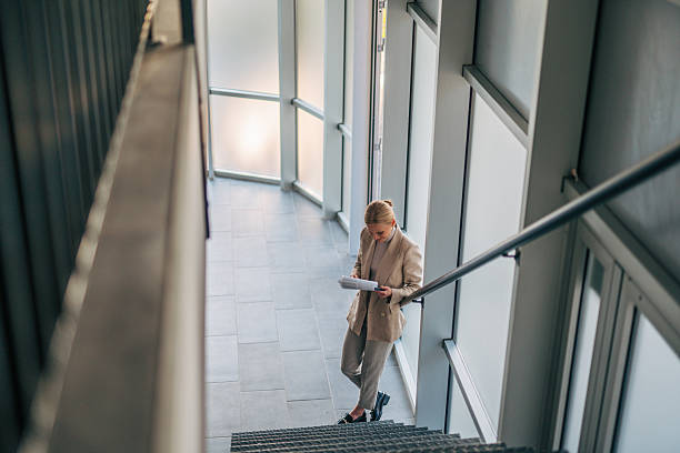istock Businesswoman reading documents while walking down office stairs 2216524016