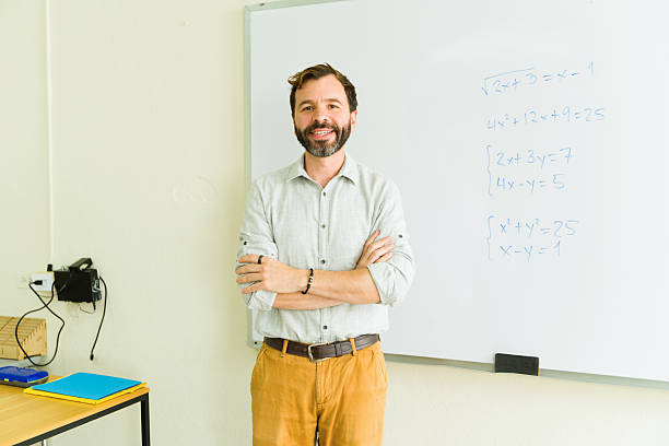 istock Smiling teacher standing in classroom with arms crossed by whiteboard with math equations 2216529853