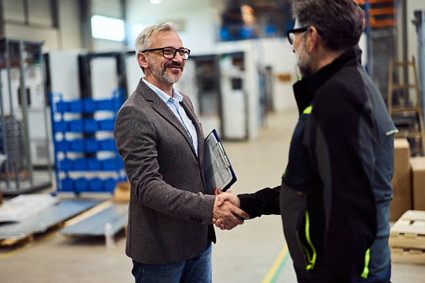 Business Professionals Shaking Hands in a Factory Setting Showing Agreement stock photo