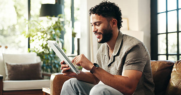istock Typing, relax and tablet with man on sofa in lounge for networking app, social media post and chat. Connection, download and update with person in living room of home for reading, scroll and update 2216533535