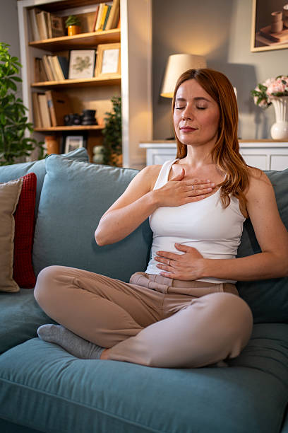 istock Serene woman practicing deep breathing exercise on sofa at home 2216539753