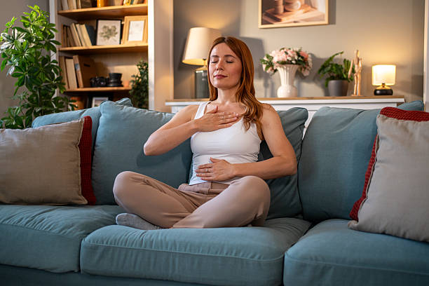 istock Serene woman practicing deep breathing exercise on sofa at home 2216539796