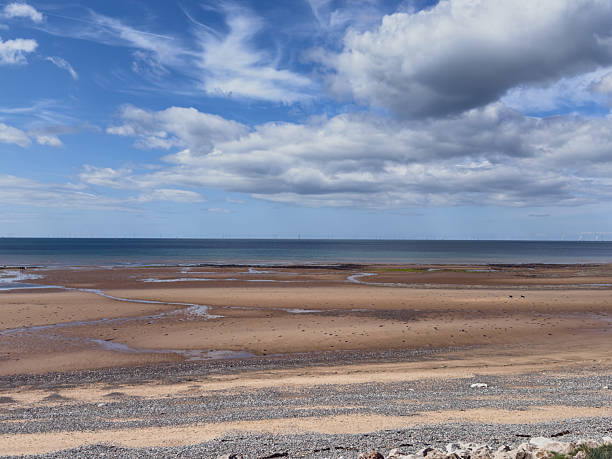 Expansive shoreline view with dramatic sky, sandy beach, and distant sea horizon on a sunny day