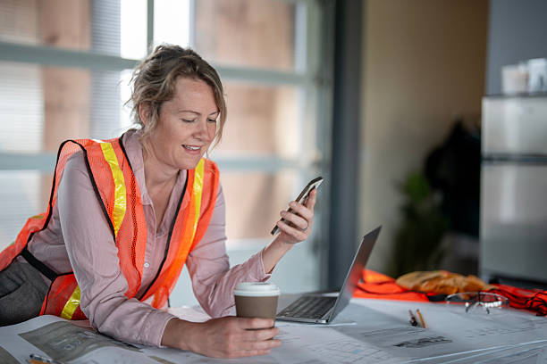 istock Female Architect Reviewing Plans and Messages at Construction Office 2216540244