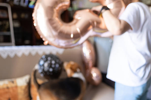 Person is setting up rose gold number balloons for a birthday party, creating a festive atmosphere with blurred foreground and background