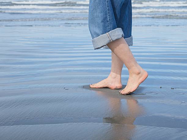 A closeup conceptual photos of a woman's feet shown barefooted walking on the beach by the pacific ocean in Washington.