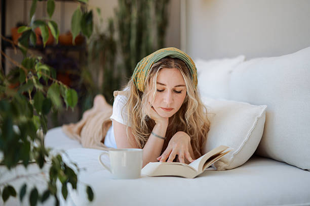istock Young woman lying on a sofa reading a book and drinking coffee 2216551126