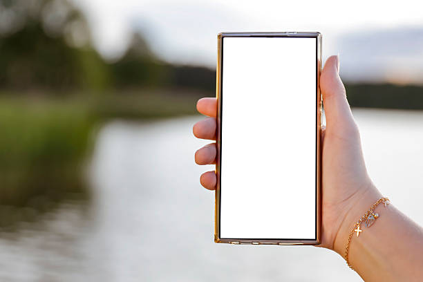 istock Woman hand holding a phone with blank white screen with copy space. In the background blurred lake and sky. 2216552532