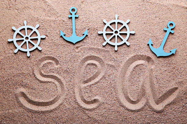Word Sea drawn on beach sand with anchor and ship wheel