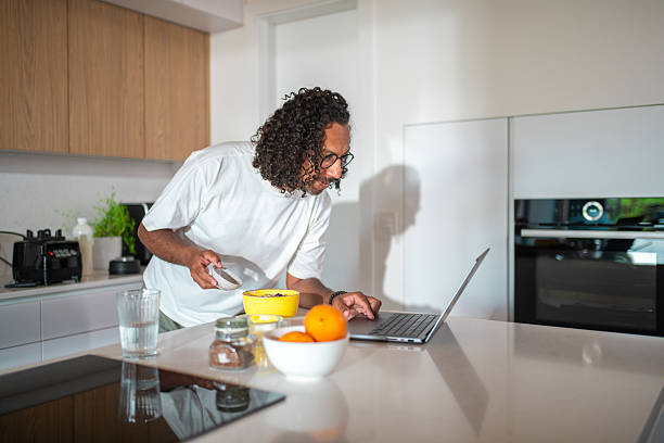 istock Mid Adult Hispanic Male Making Smoothie at Home While Using Laptop in Modern Kitchen 2216553737
