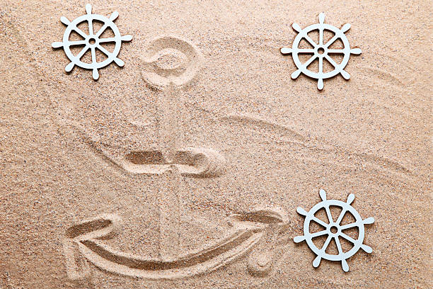Anchor drawn on beach sand with ship wheel